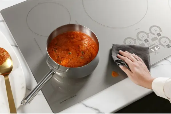 A woman cleaning the surface of the Monogram ZHU30RSTSS 30” induction while cooking 