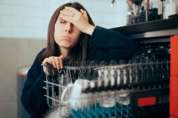 A woman pouting next to an open dishwasher
