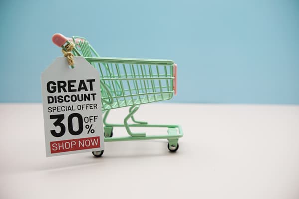 A miniature green shopping cart with a sale tag against a blue background 
