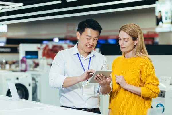 A salesman showing a woman in a yellow sweater something on a tablet 