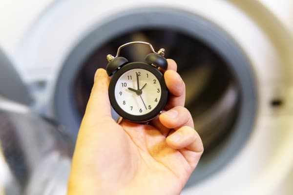 A person holding a miniature analog alarm clock with a front load washer in the background
