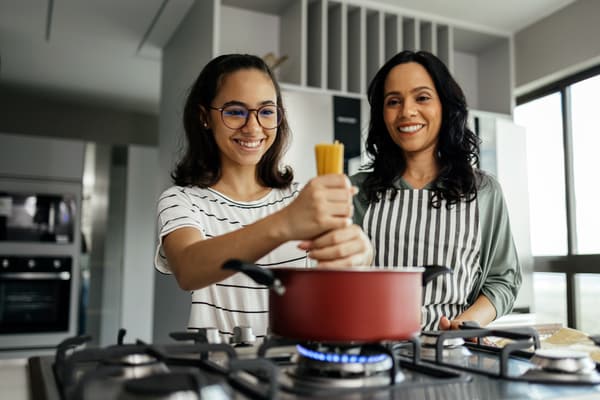 A mother and a daughter cooking pasta in a red pot