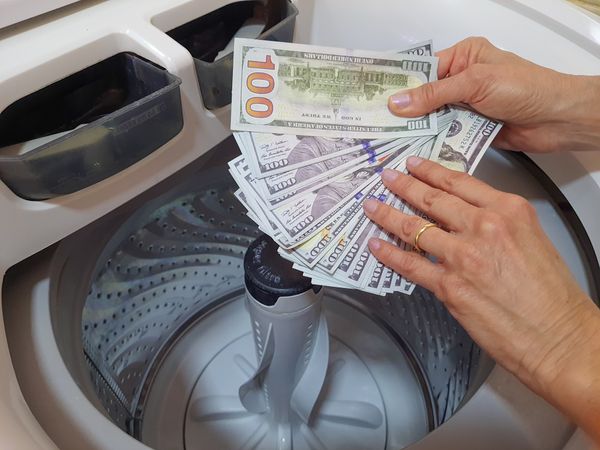 iStock Credit: Elis Cora A person inserting $100 bills in a top load washer