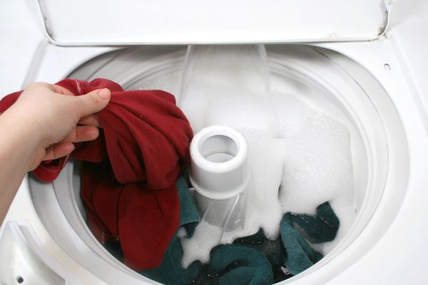 A person adding clothes to a top load washer 