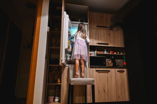 A child on a chair looking into a refrigerator 