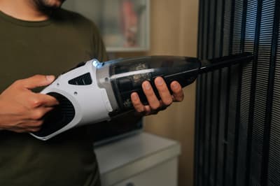 A person vacuuming refrigerator coils 