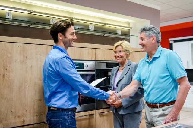 Credit: iStock Front view of a salesman shaking hands with a man and woman in an applinace store