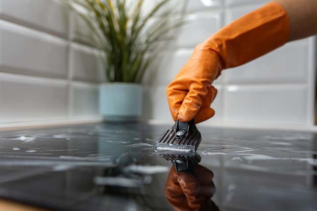 View of a person cleaning an induction cooktop with a scraper View of a person cleaning an induction cooktop with a scraper