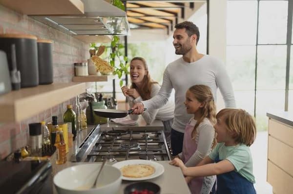 A family smiling while cooking around a stove A family smiling while cooking around a stove