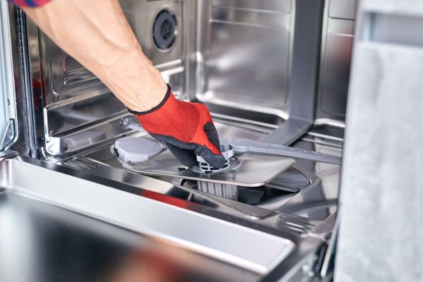 An appliance technician removing a dishwasher filter