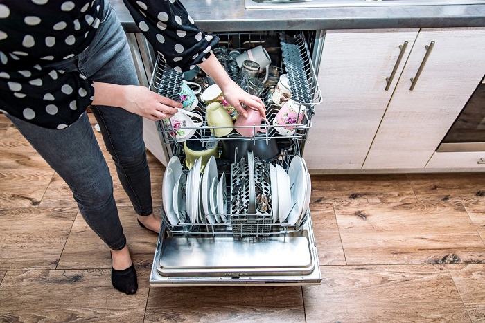 Woman unloading dishwasher with both washer racks pulled out.