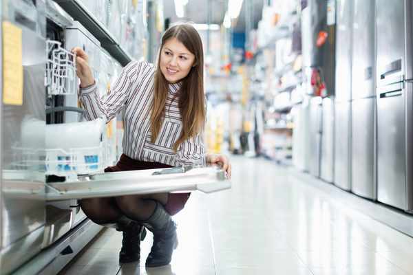 A woman crouching to inspect a dishwasher