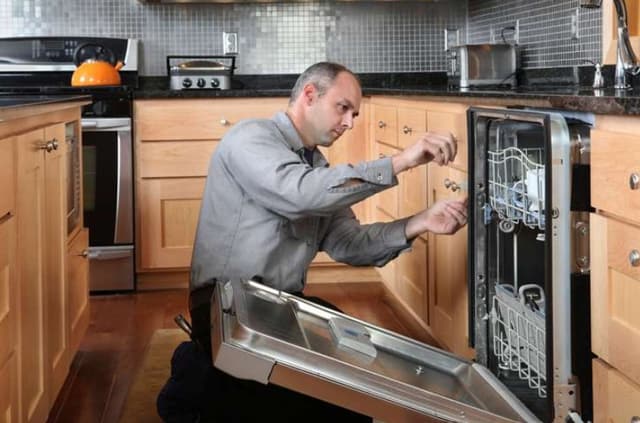 Front view of a man installing a new dishwasher Front view of a man installing a new dishwasher