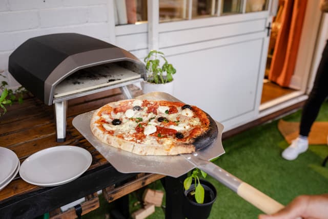 Front view of a person placing a pizza in a countertop pizza oven