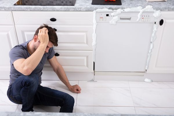 A man sitting next to a flooding dishwasher 
