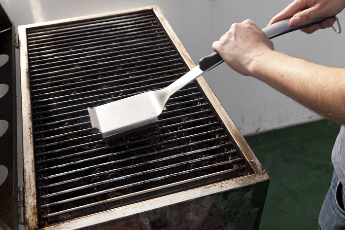 eldadcarin Man cleaning a grill with a grill scrubber.