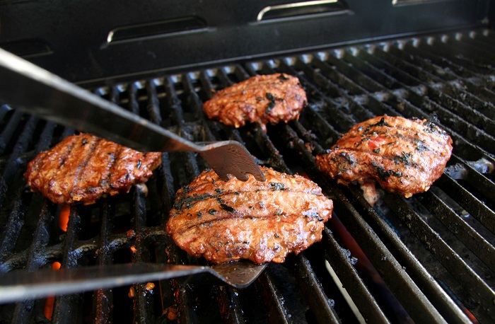 SDI Productions Four fully-cooked burgers being taken off the grill with metal tongs.