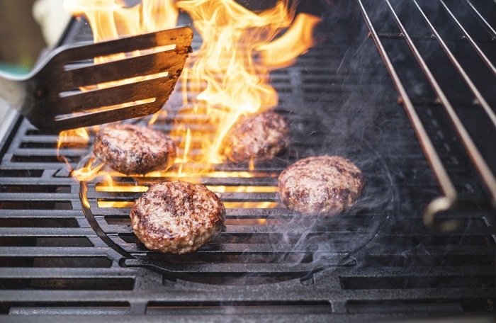 EllenMoran Four burger patties on a fiery grill with visible flames.