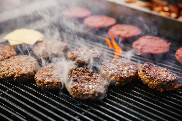 Kanawa_Studio Rows of burgers on a fiery grill with visible smoke.