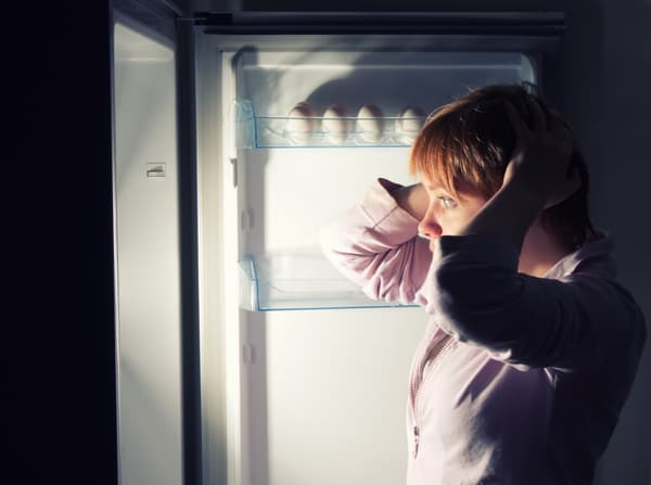 A woman holding her ears in front of an open refrigerator 