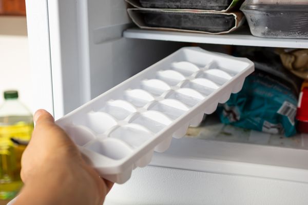 A person inserting an ice cube tray into a freezer