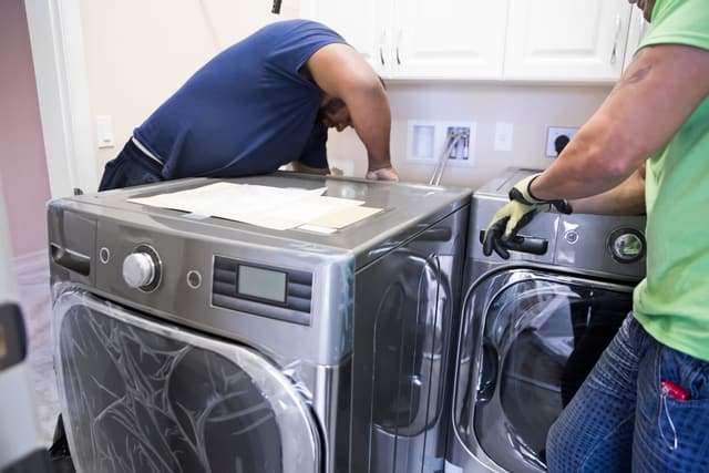 Front view of two men installing a washer and dryer in a laundry room Front view of two men installing a washer and dryer in a laundry room