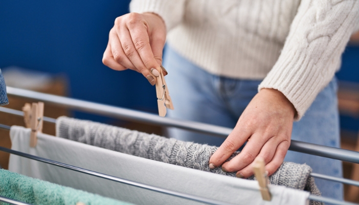 Appl_winter-laundry-tips_4.jpg A pair of hands clips laundry onto a line indoors to air dry.