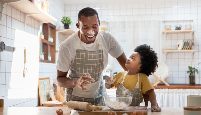 A man has flour on his face as he and a child bake in their kitchen.