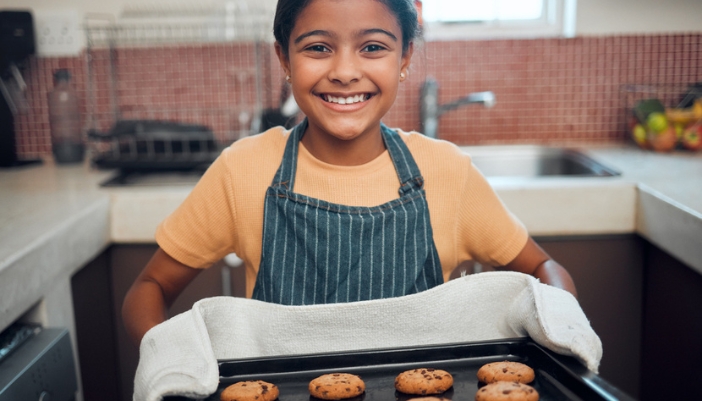 A young girl holds up a tray of cookies to the camera. 