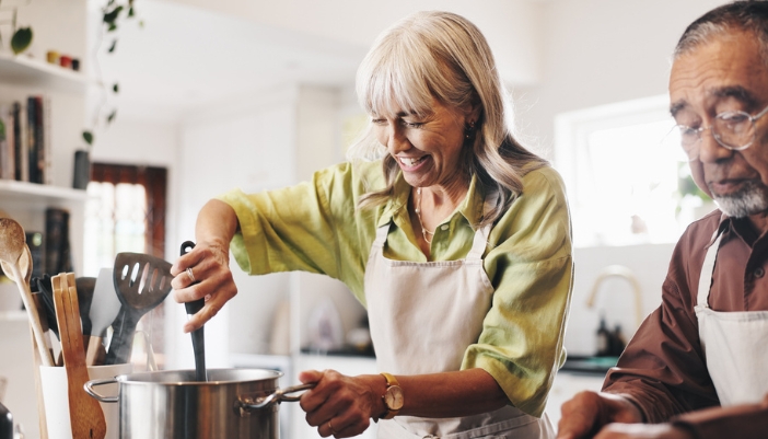 An elderly couple cook together at home.