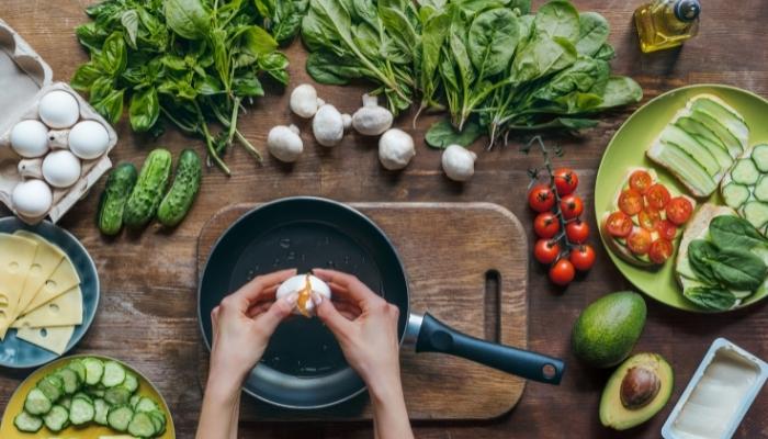 Hands cracking egg over skillet on table with ingredients