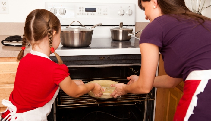 App_Cooktop-vs-Range_3.jpg Mom and daughter putting a pie in the oven on the range, with pots on cooktop