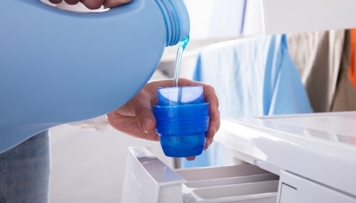 A pair of hands pour laundry detergent into a blue detergent cup.