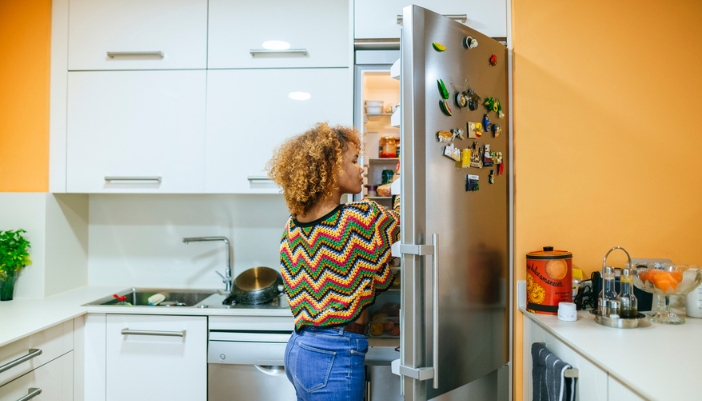 A young woman reaches into her fridge at home.