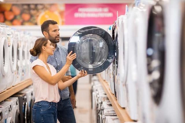 View of a couple shopping for a new washing machine in an appliance store View of a couple shopping for a new washing machine in an appliance store