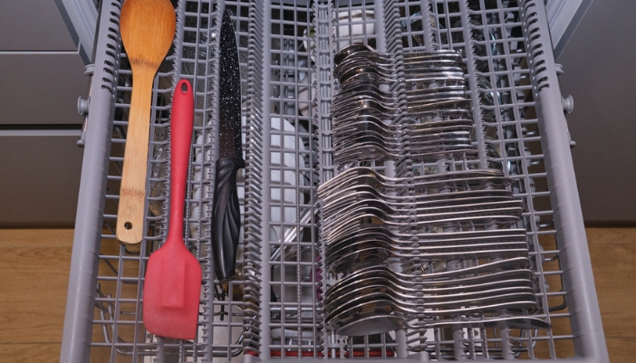 A woman loads a stock pot cover into the lower rack of her dishwasher.