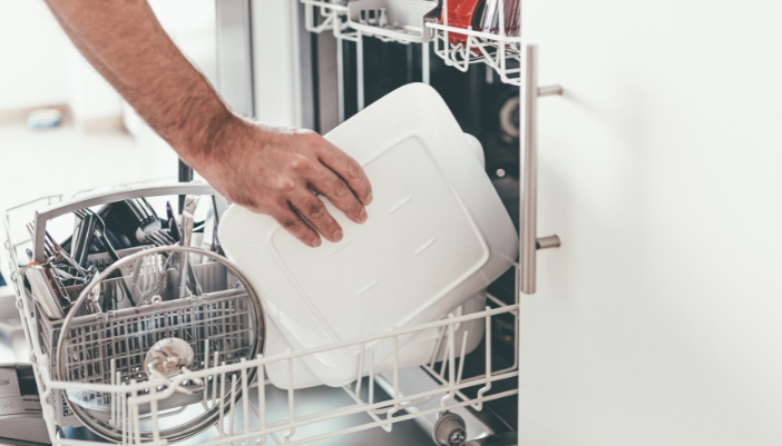 Bottom rack of a dishwasher being loaded with dinner plates angled toward the spray arm