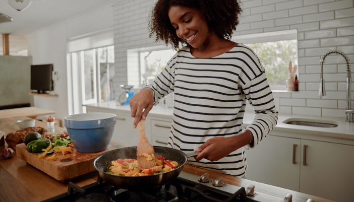 A young woman cooks in a skillet in her modern home kitchen.