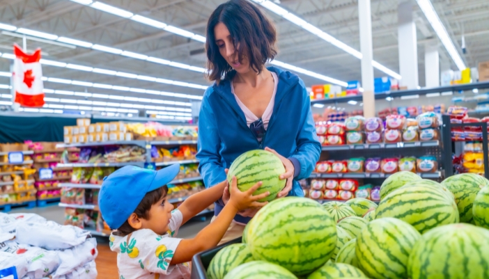 A mom and son pick out a watermelon at a grocery store.