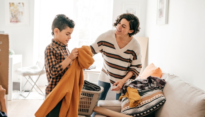 Mother and son folding a few pieces of fresh laundry together in a sunny living room
