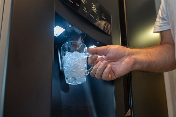A close-up of a person using a refrigerator ice dispenser