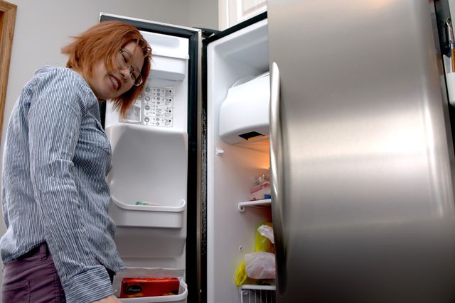 Credit: iStock View of a woman looking inside her garage ready refrigerator and smiling
