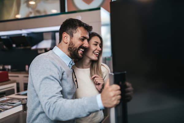 iStock Credit: Group4 Studio A smiling woman and man inspecting a refrigerator in a store