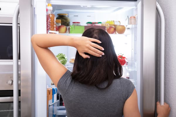A woman scratching her head in front of an open refrigerator