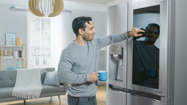 A smiling man using a touchscreen refrigerator 