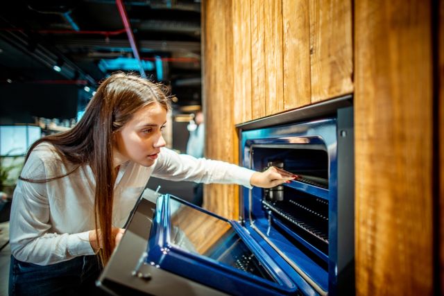 Side view of a woman examining a wall oven in an appliance store