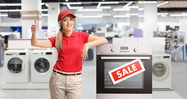 A saleswoman giving a thumbs up next an oven with a sale sign