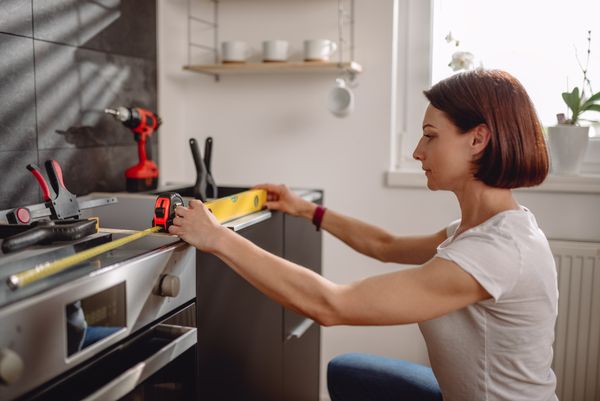 A woman using a leveling tool on kitchen cabinets 