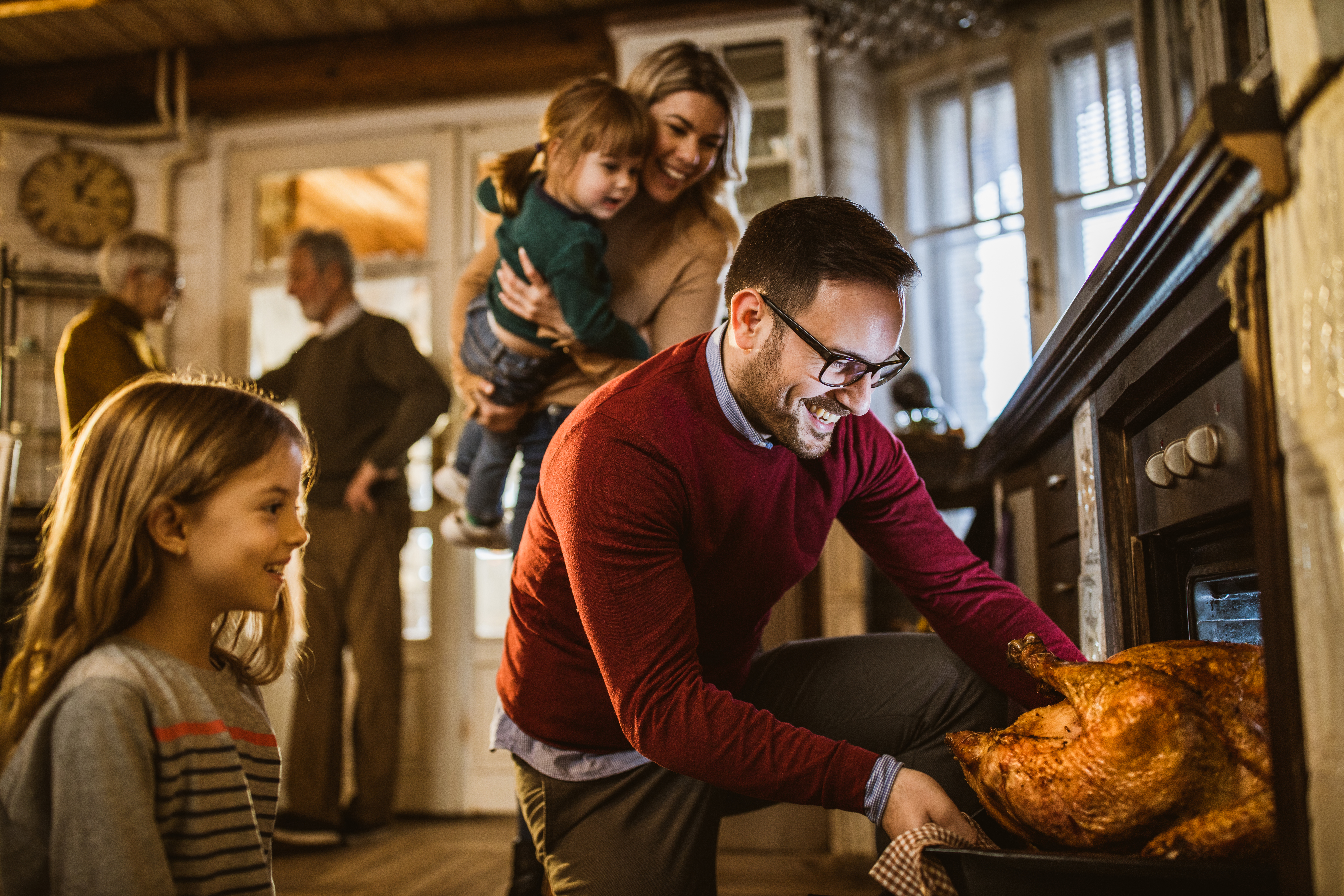 kynesher A man pulls out a turkey from the oven while family gathers around