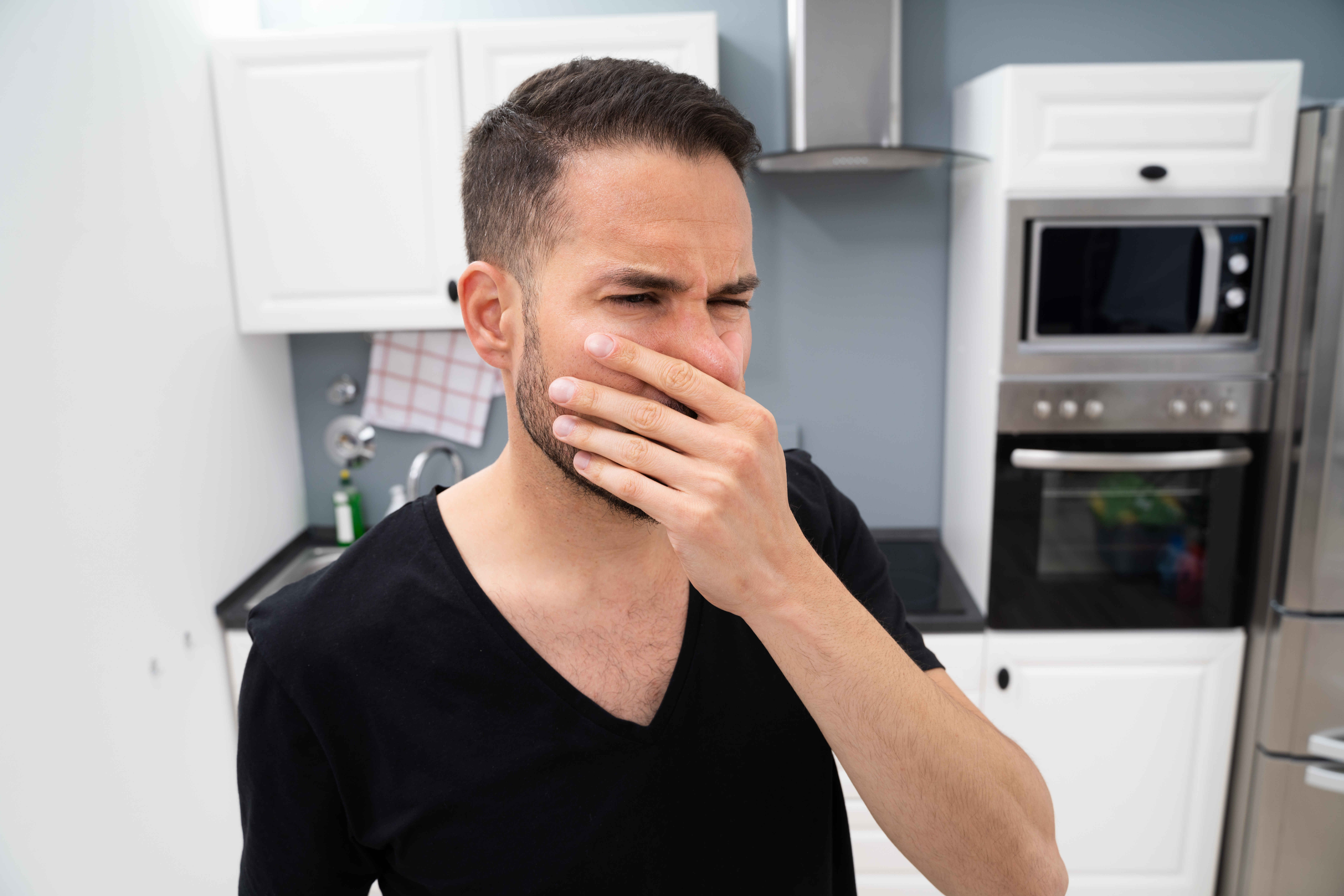 AndreyPopov Man in a black shirt covering his nose in disgust in a kitchen